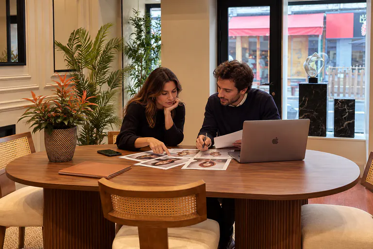 Deux personnes travaillent sur des photos imprimées, devant une vitrine sur rue