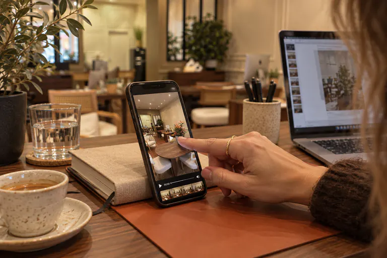 Main faisant défiler des photos sur un smartphone, à côté d'un ordinateur portable