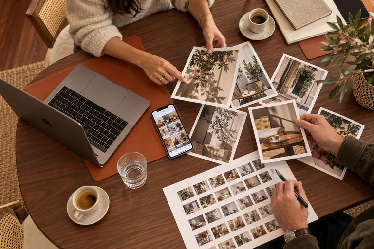 Vue de dessus : des mains trient des photos imprimées à côté d'un ordinateur et d'un café
