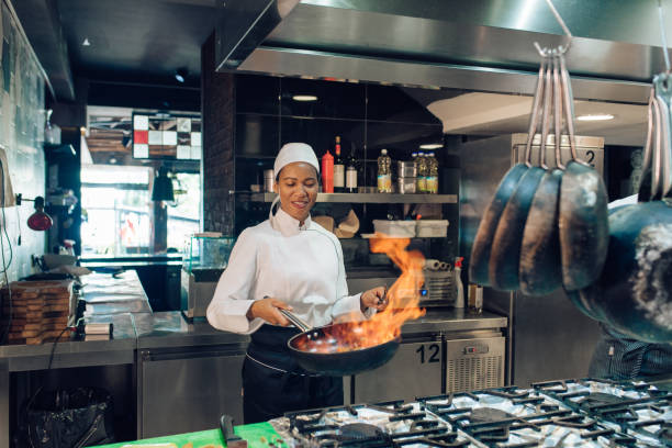 Female chef from the restaurant kitchen is cooking a flambé specialty. agence SEO cuisiniste à Lyon