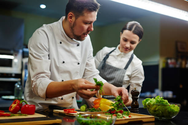 Chef consulting his trainee while cooking salad services web cuisiniste à Lyon