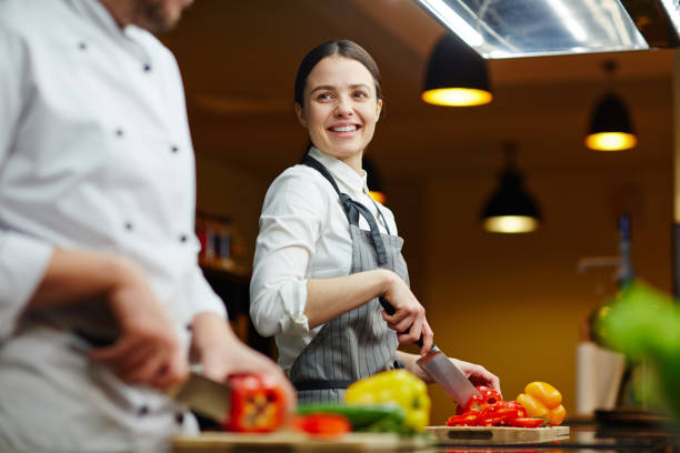 Smiling trainee talking to expert while cutting raw pepper agence web cuisiniste à Lyon