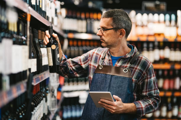 Mid adult man checking the stock of wine in liquor section of a supermarket Agence SEO comptable Lyon