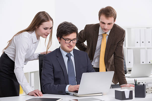 Three businesspeople at one laptop, office background. Concept of team work. agence web La Mulatière